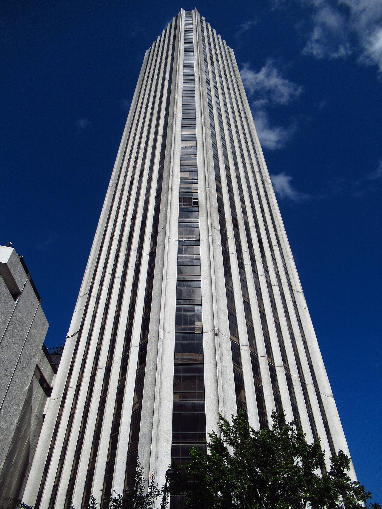 The Torre Colpatria office tower in Bogotá seen from street level, its white vertical ribs rising against a deep blue sky