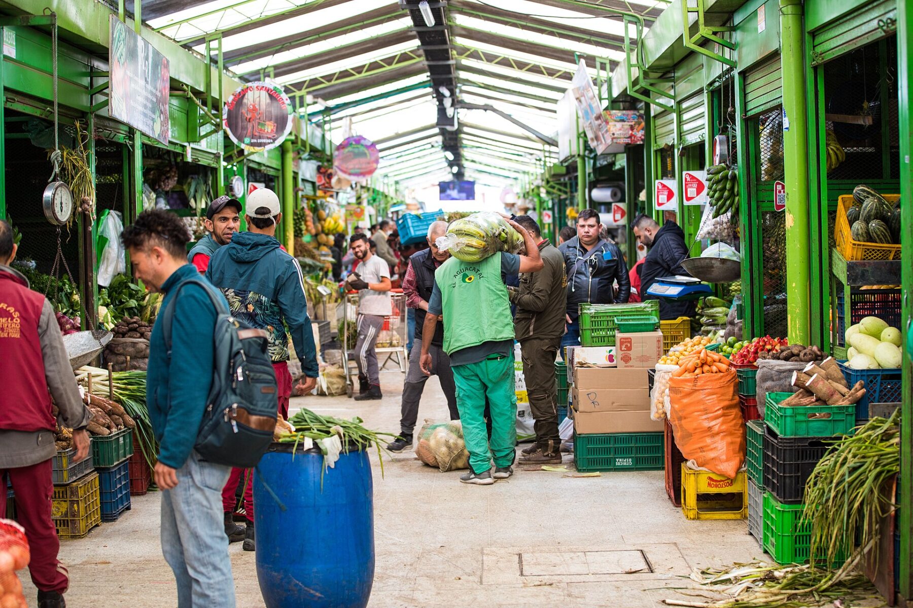 A porter carries a sack of plantains past stalls of potatoes, carrots, cassava and fruit at the Paloquemao market in Bogotá, Colombia