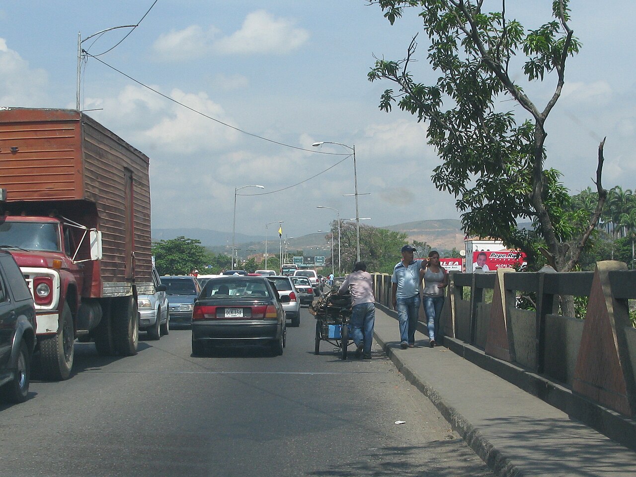Cars, a lorry, a man pushing a cart and pedestrians crossing the Simón Bolívar International Bridge between Venezuela and Colombia