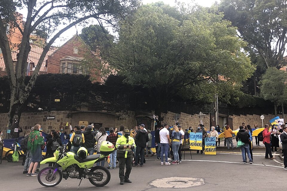 People gather outside the walls of the Russian embassy in Bogotá, Colombia, watched by a police officer