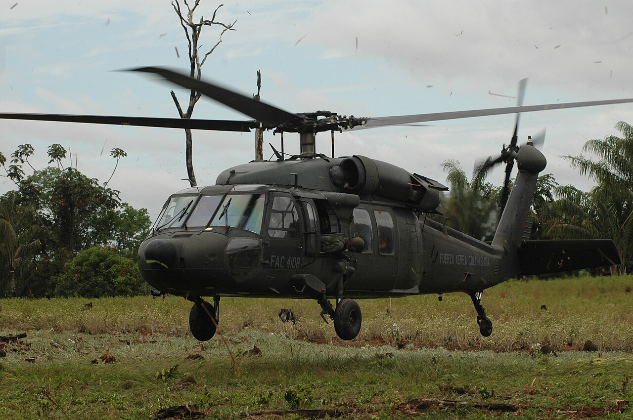 A Colombian Air Force Black Hawk helicopter landing in a grassy field next to tropical trees