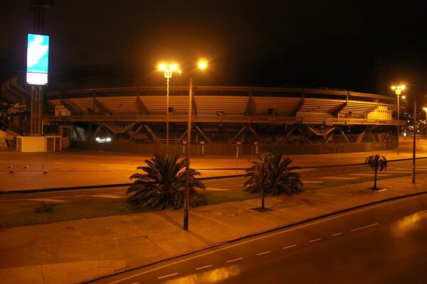 Estadio El Campín in Bogotá, Colombia, lit by street lamps at night, seen from across the road