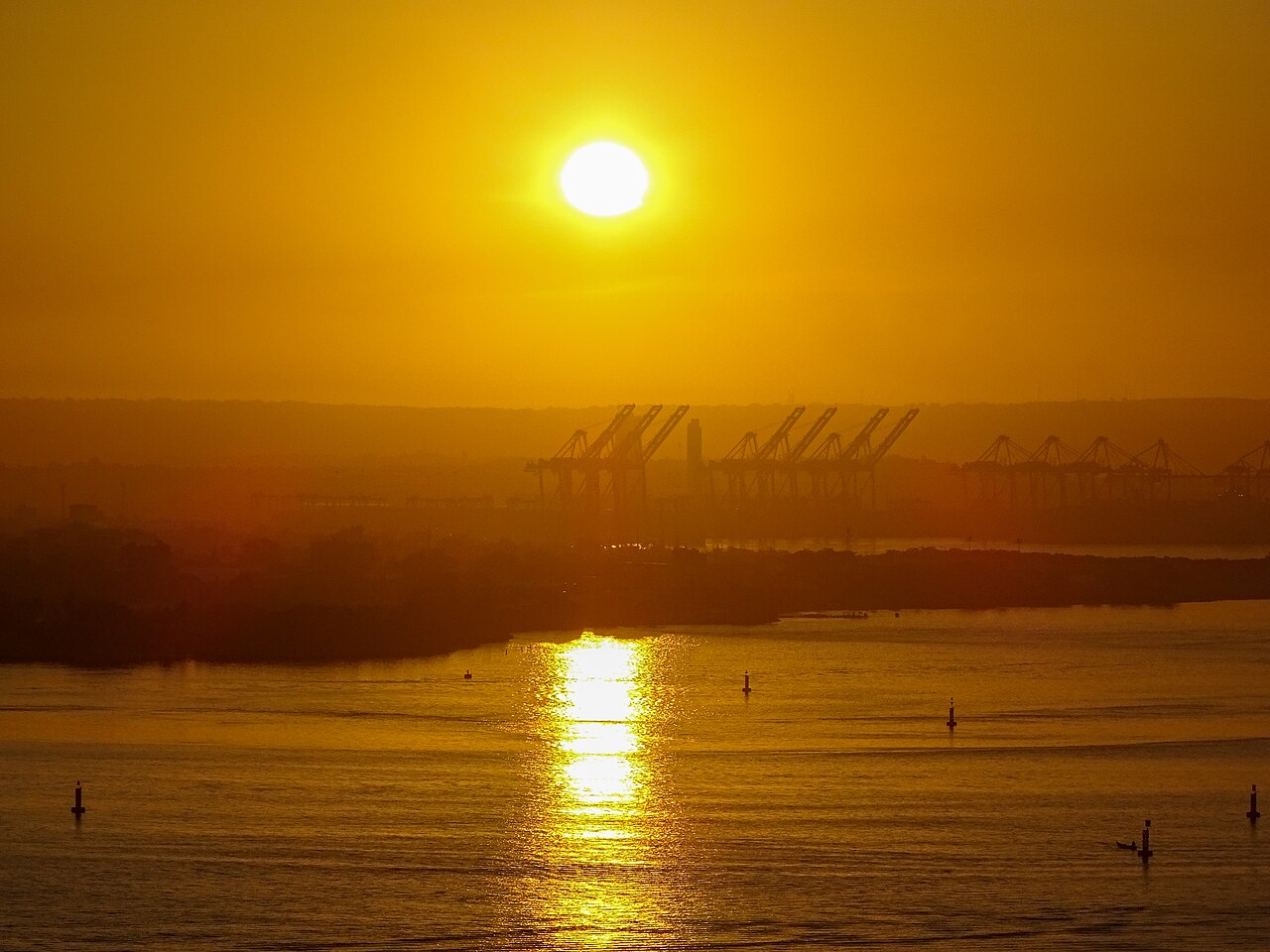 Silhouetted container cranes at the commercial port of Cartagena, Colombia, under an orange sunrise sky