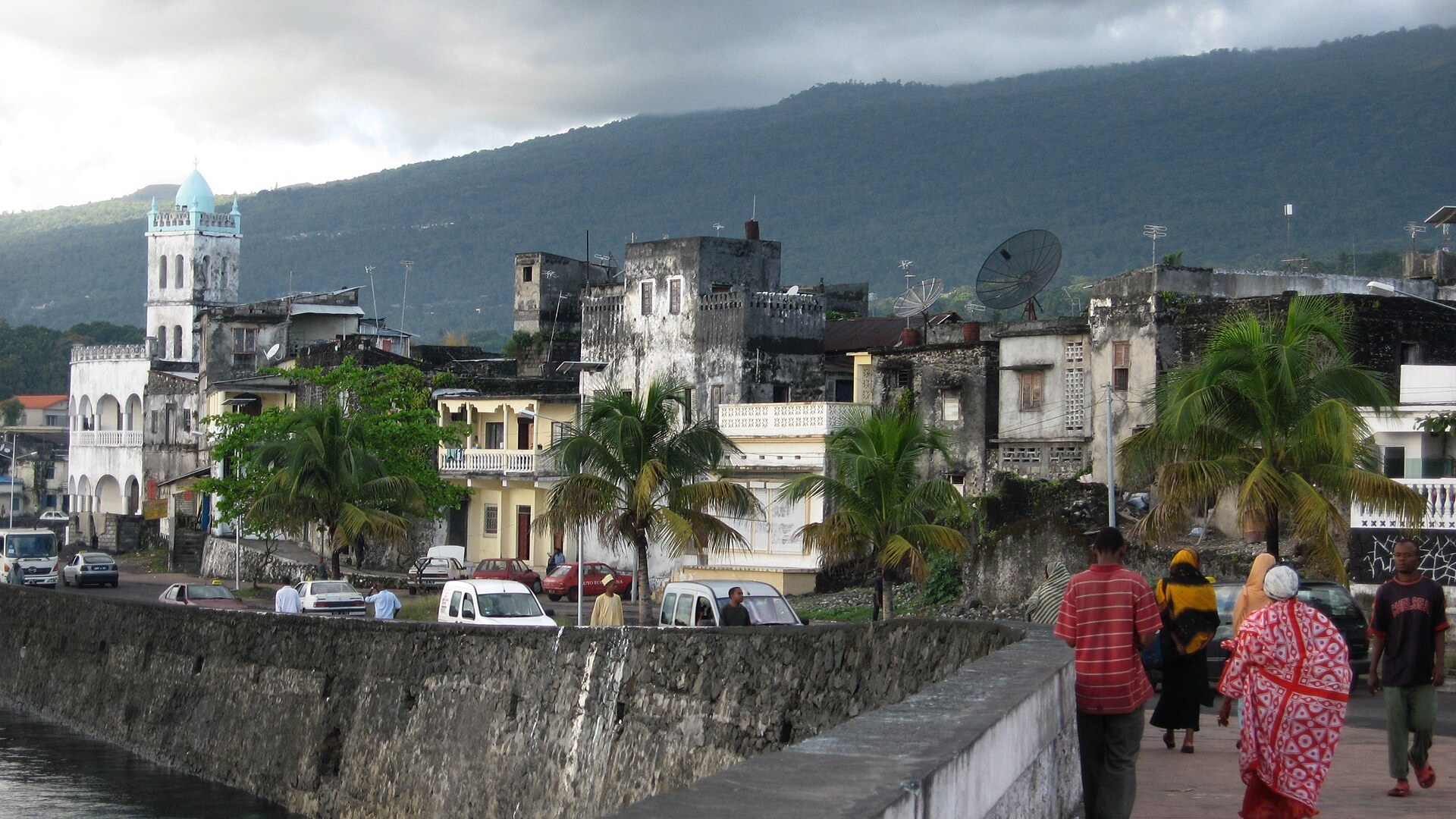 Seawall and waterfront houses of Moroni harbour on Grande Comore with a mosque tower and a forested hillside behind