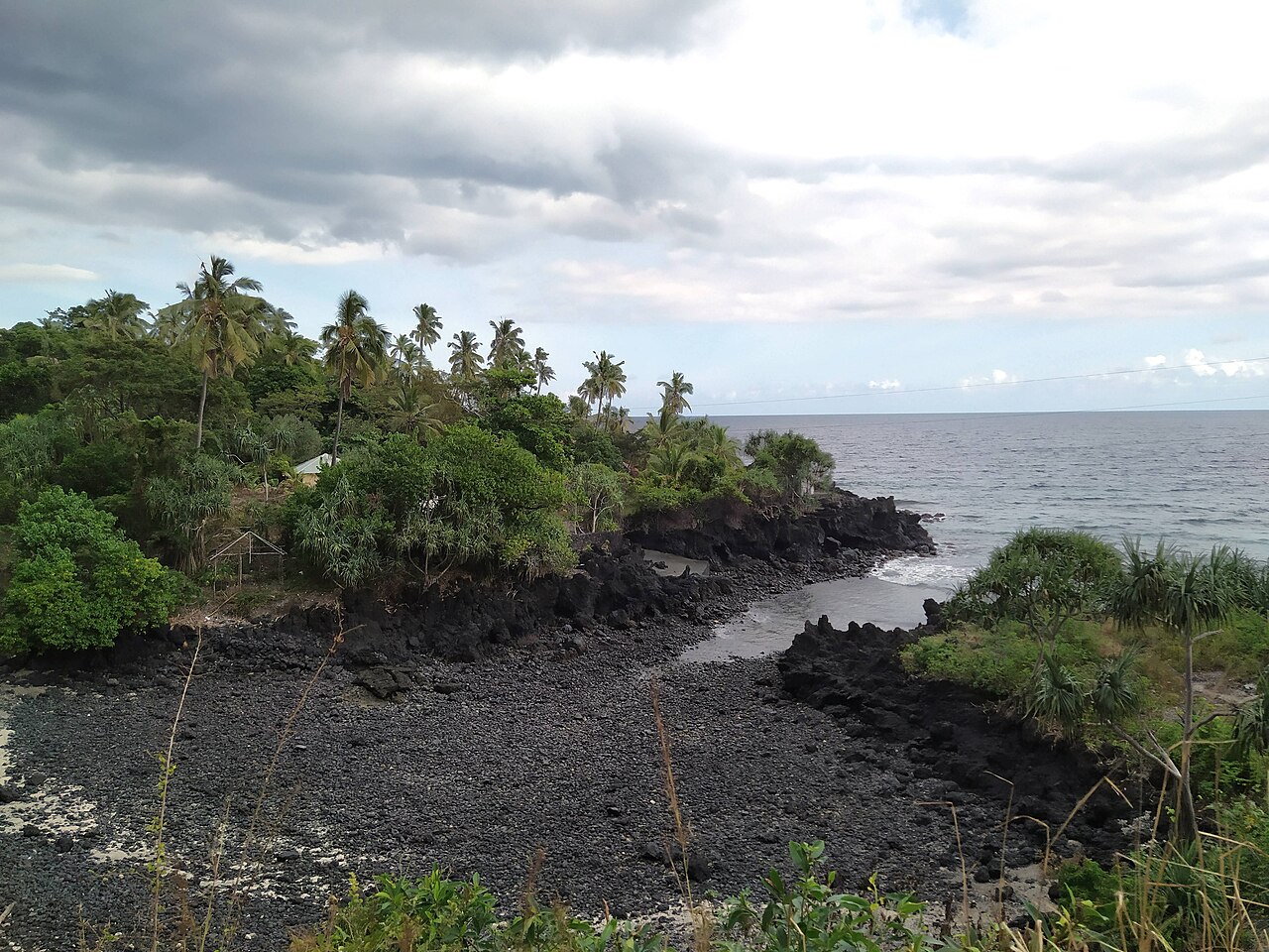 A cove of black volcanic stones and rock framed by coconut palms on the west shore of Grande Comore