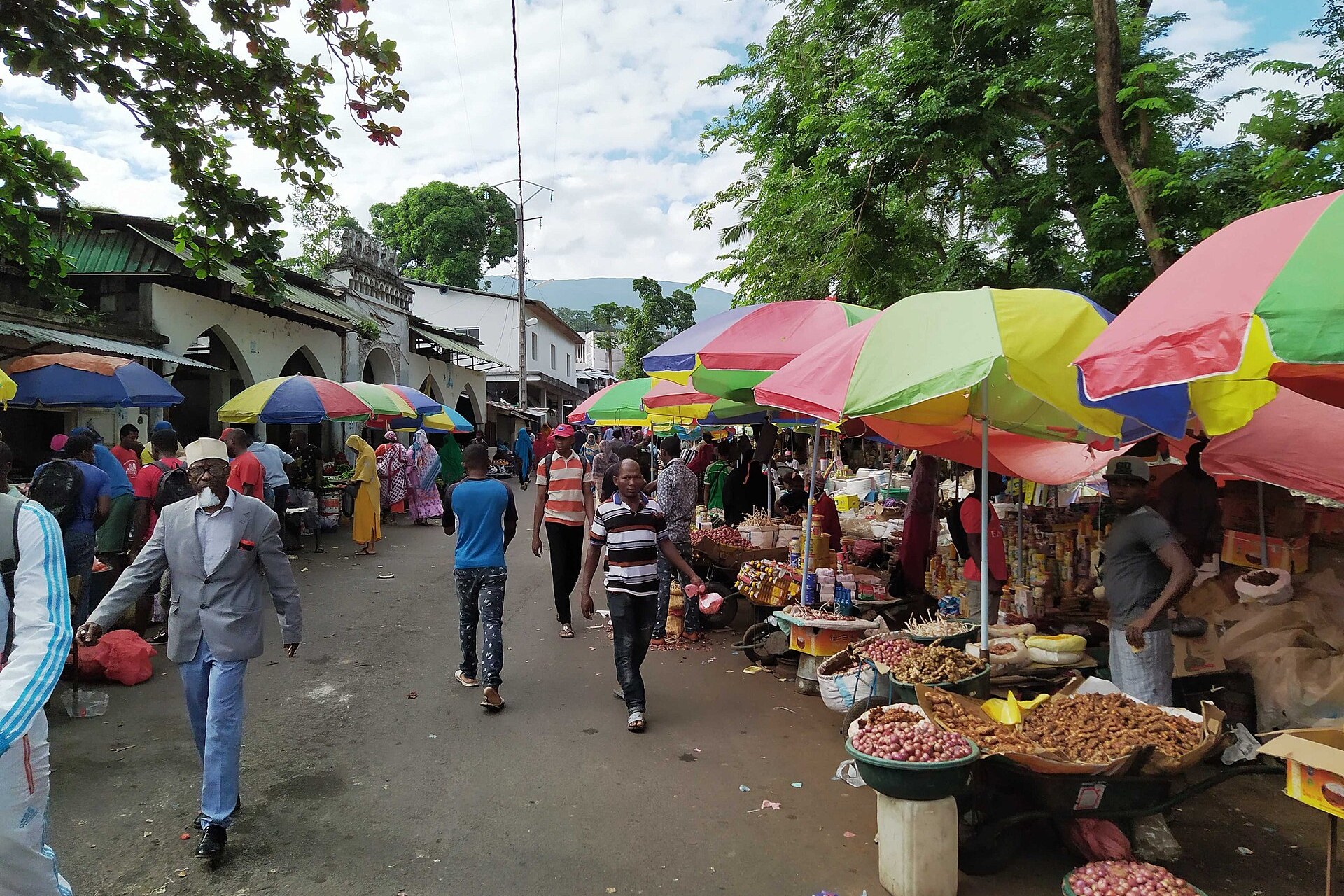 Shoppers walk past market stalls under colourful umbrellas on a street in Moroni, capital of the Comoros