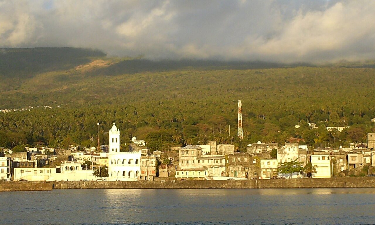 Waterfront of Moroni, Comoros, with a white mosque tower and houses below forested hills