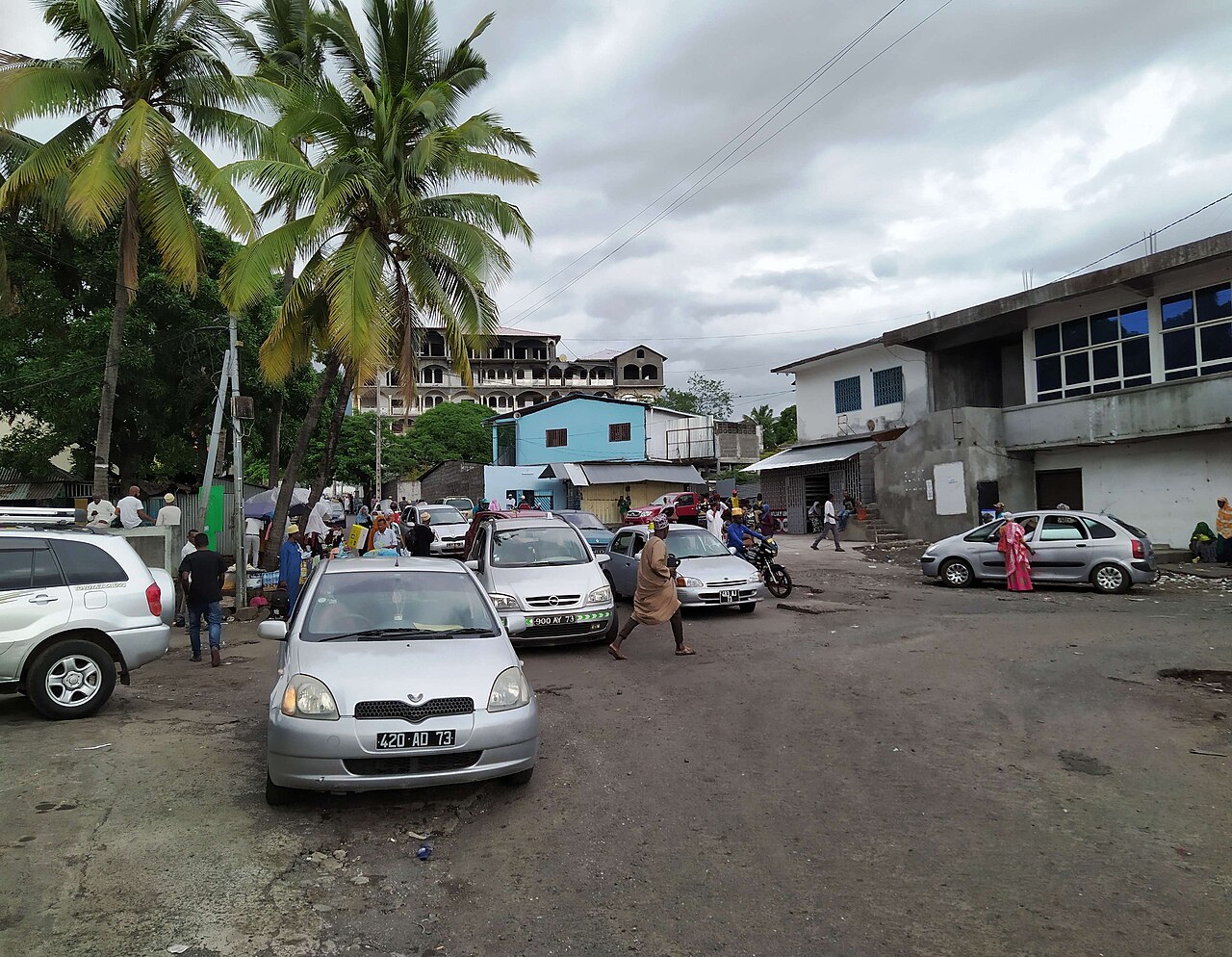 Cars, motorbikes and pedestrians gather at a street junction under coconut palms in Moroni, Comoros
