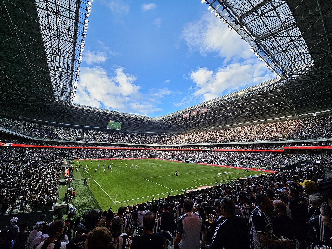 Supporters in black and white fill the stands of the Arena MRV in Belo Horizonte during an Atlético Mineiro game, under the stadium's ring-shaped roof.