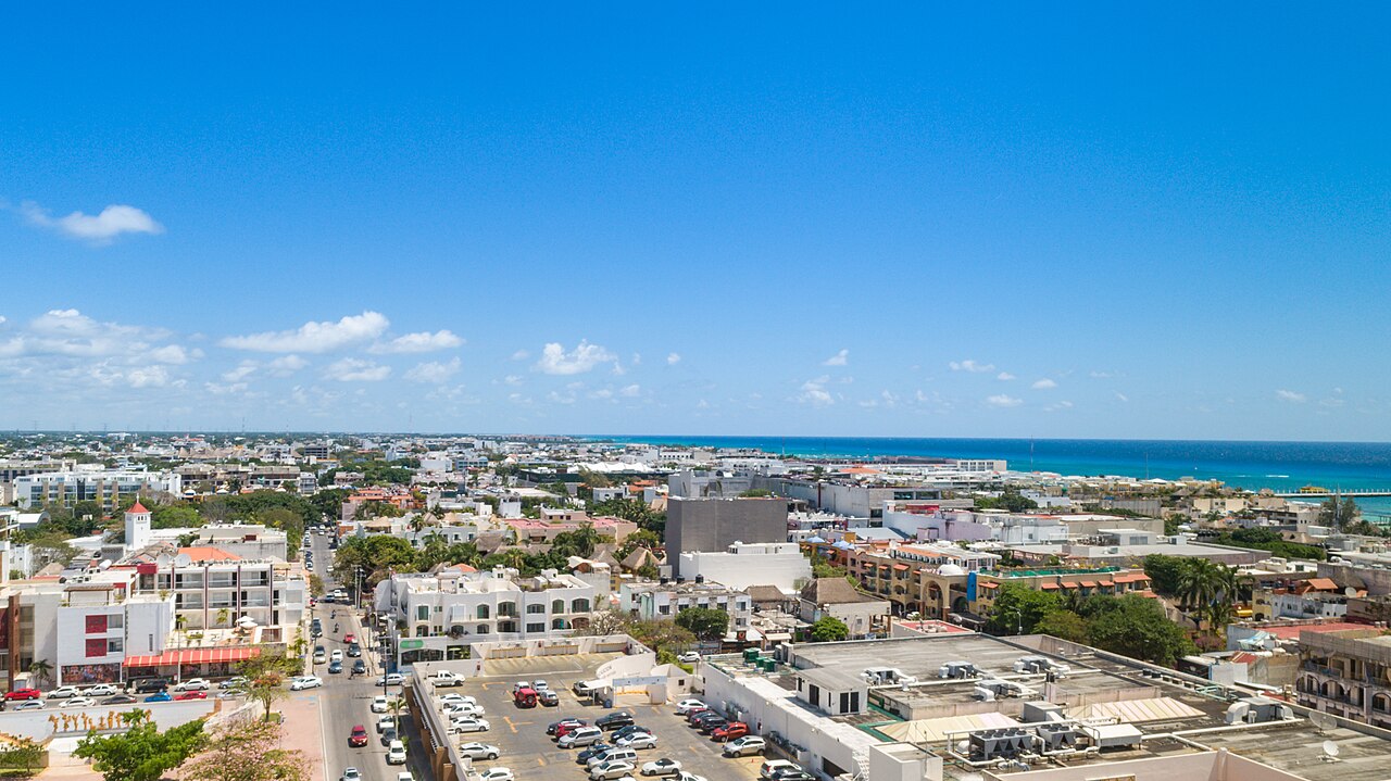 Aerial view of Playa del Carmen, Mexico, with low white buildings, a main street and the Caribbean Sea on the horizon