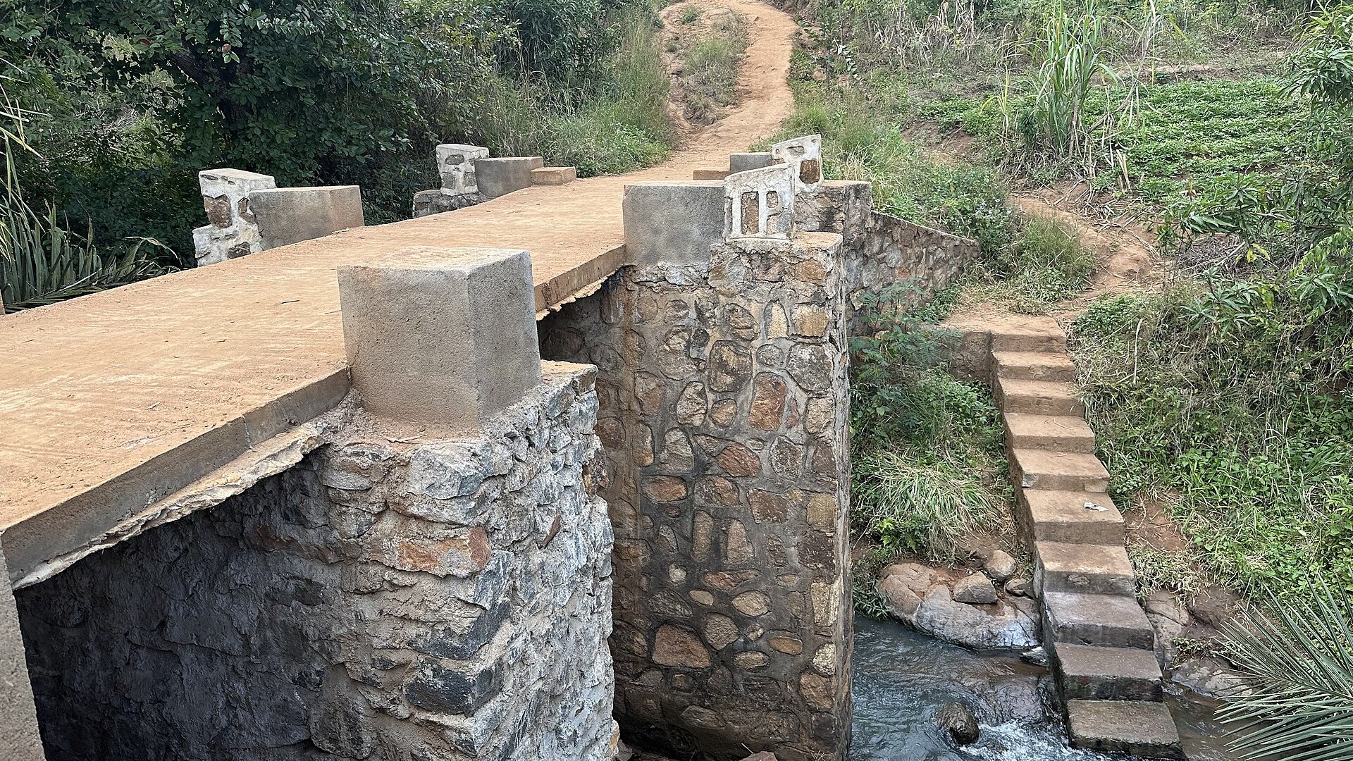 Small stone and concrete bridge over a stream with a dirt path leading uphill at Thondwe in Malawi