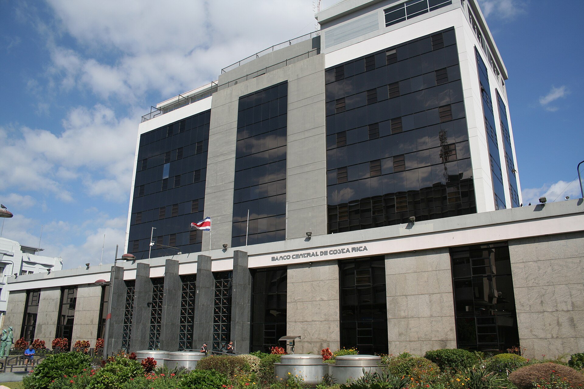 Glass and granite Banco Central de Costa Rica building with its name on the facade and a Costa Rican flag in San Jose