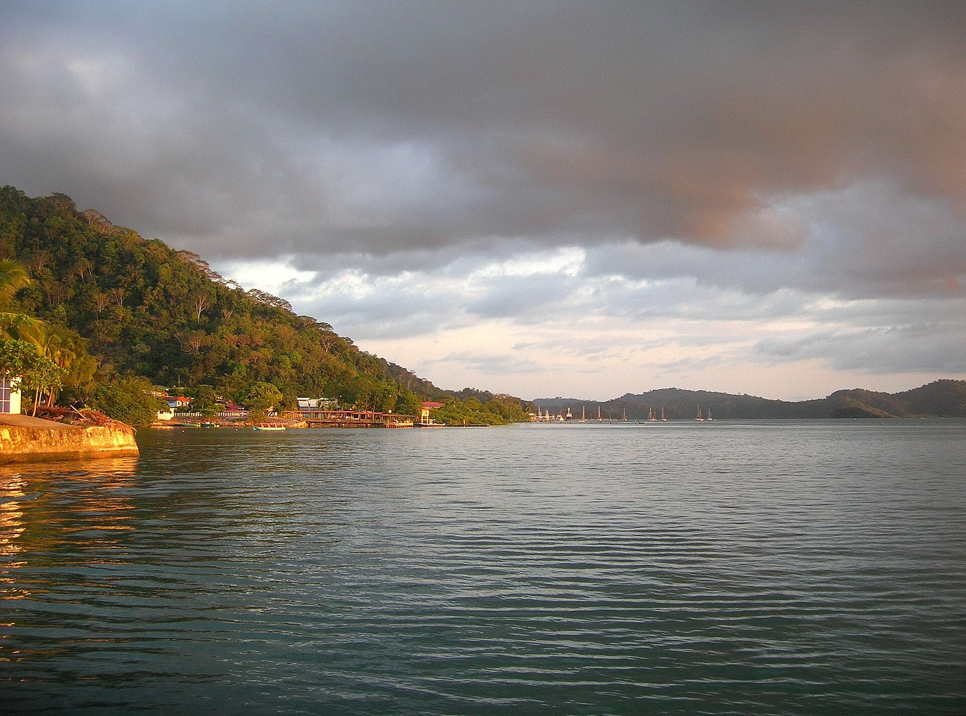 Golfito bay in southern Costa Rica at dusk under cloudy skies with forested hills and moored boats