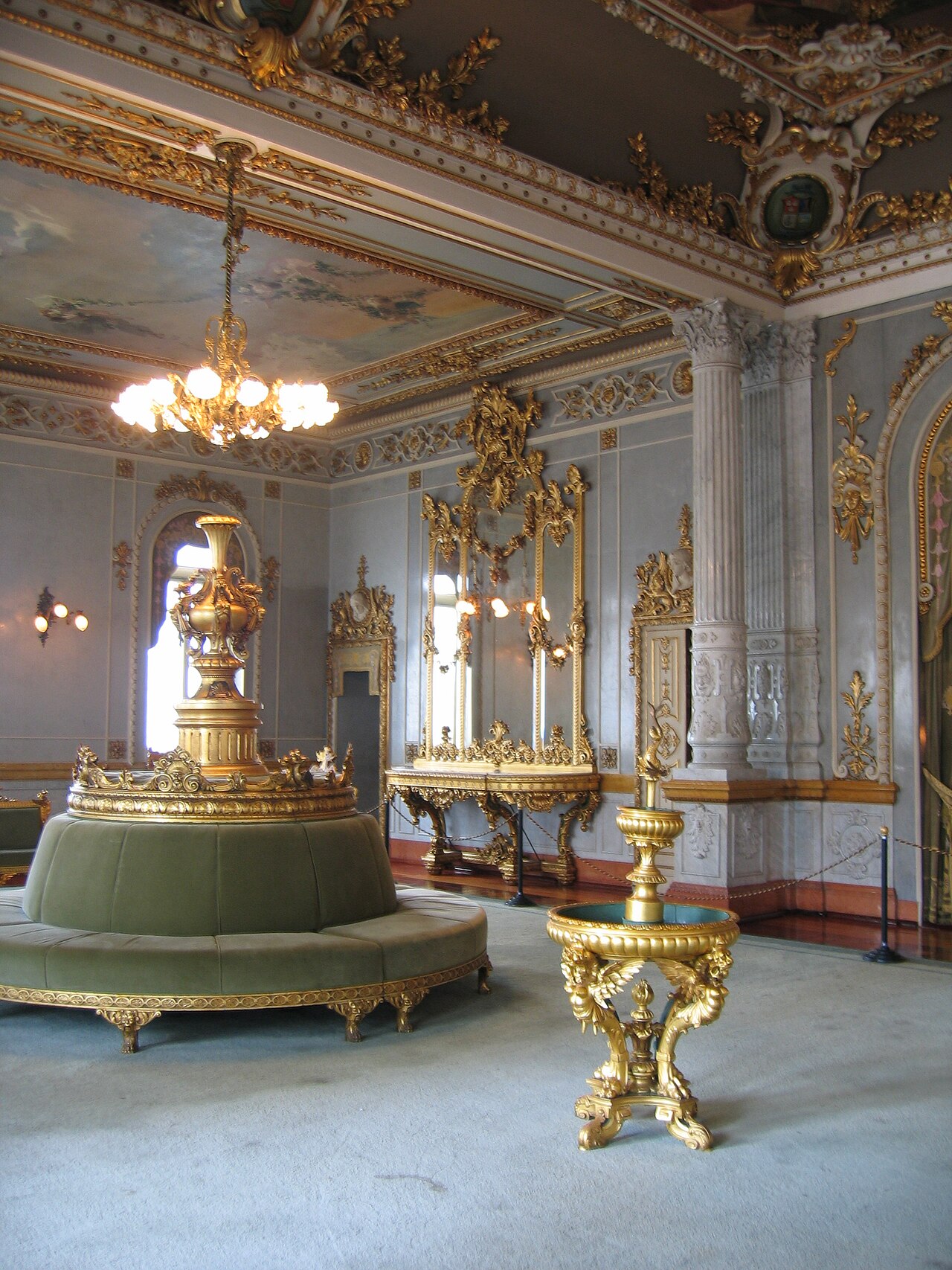 A gilded salon with a chandelier, painted ceiling, mirrors and a round green velvet sofa inside the National Theatre of Costa Rica.