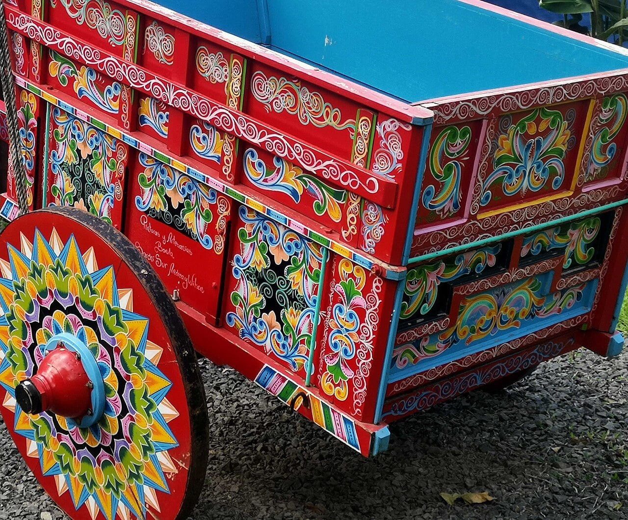 A red Costa Rican oxcart with a star-patterned wheel and painted floral panels in blue, green and yellow.