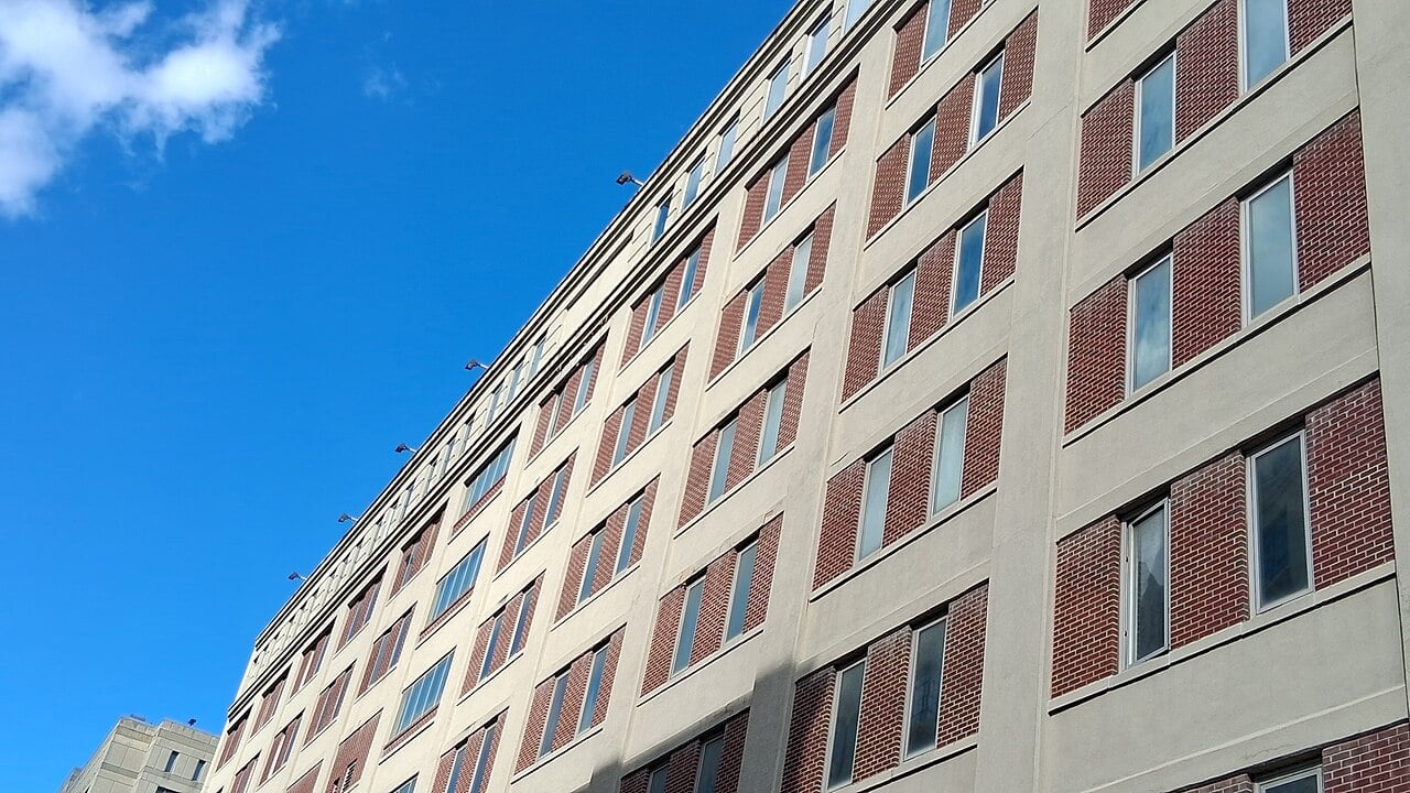 A tall beige and red-brick federal detention building with rows of windows rises against a blue sky