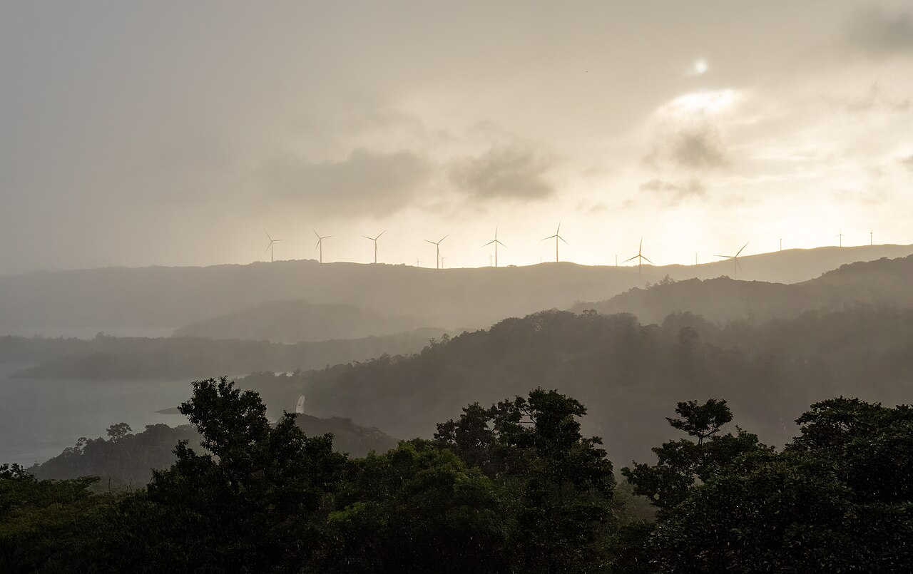 Wind turbines on a hill ridge above forest and Lake Arenal in morning mist, Costa Rica.