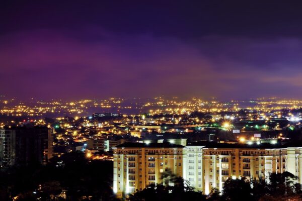 Night view of the Escazú area of San José province, Costa Rica, with city lights spread across the valley and a lit apartment block in the foreground under a purple sky
