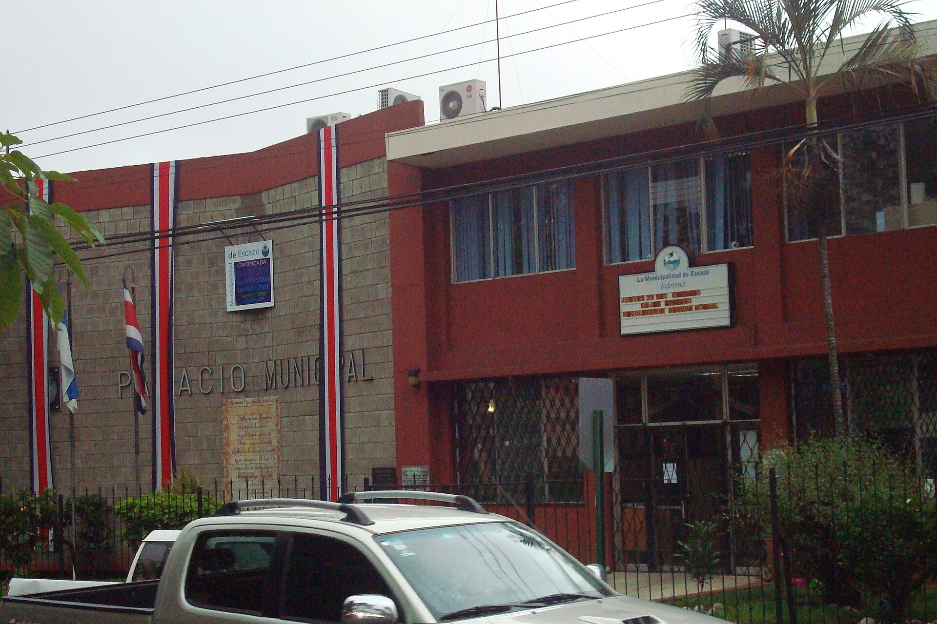 The Palacio Municipal, the municipal building of Escazú, Costa Rica, with Costa Rican flag ribbons on its brick facade and a parked pickup truck in the foreground