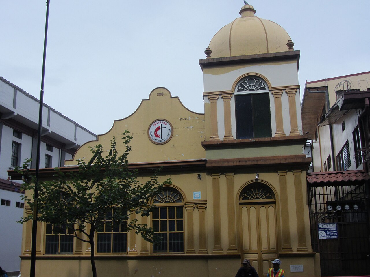 Yellow facade of the Iglesia Metodista El Mesias in Alajuela, Costa Rica, with a domed tower and arched windows