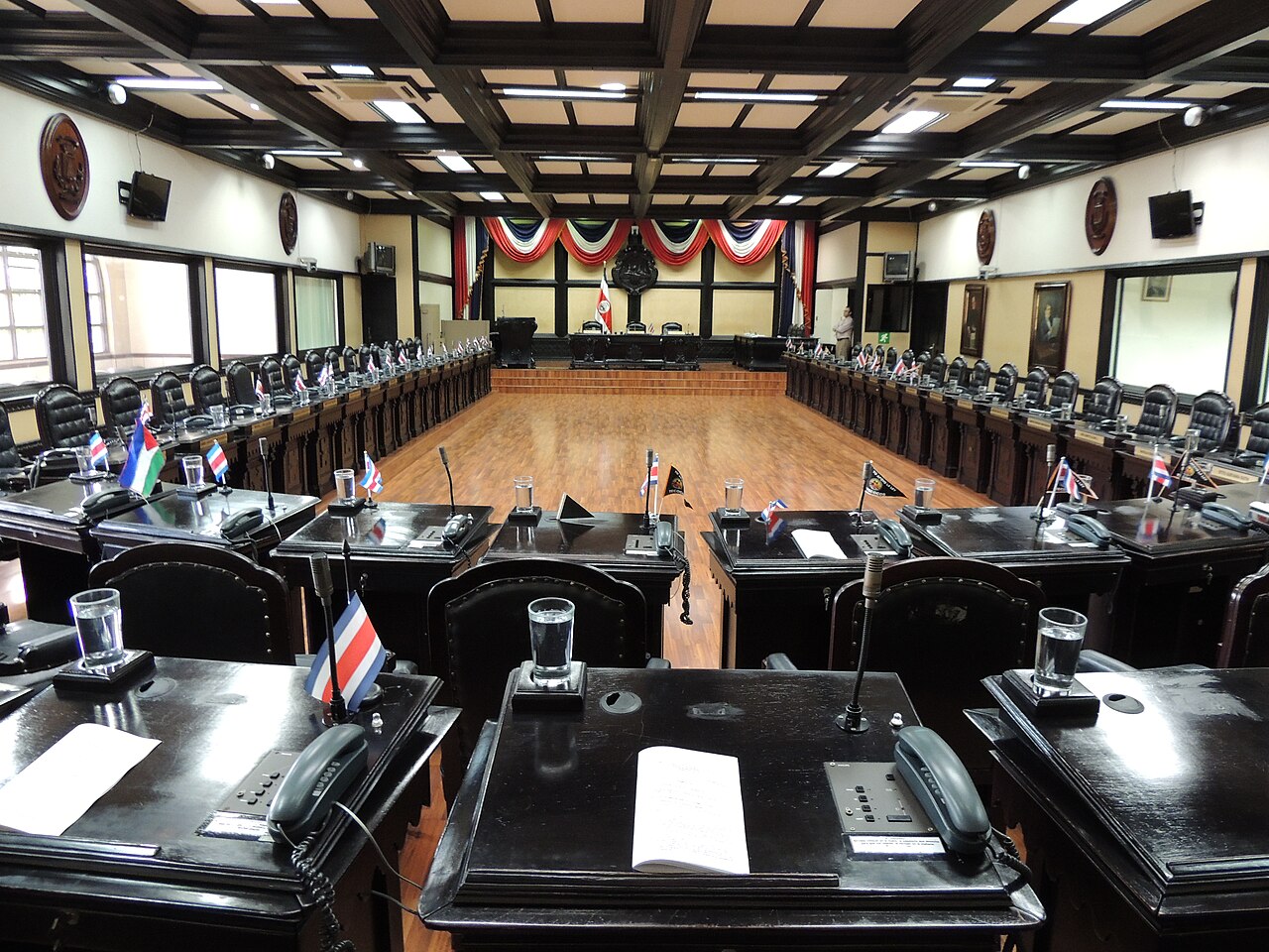 Empty deputies' desks with small Costa Rican flags in a plenary chamber of the Legislative Assembly in San José