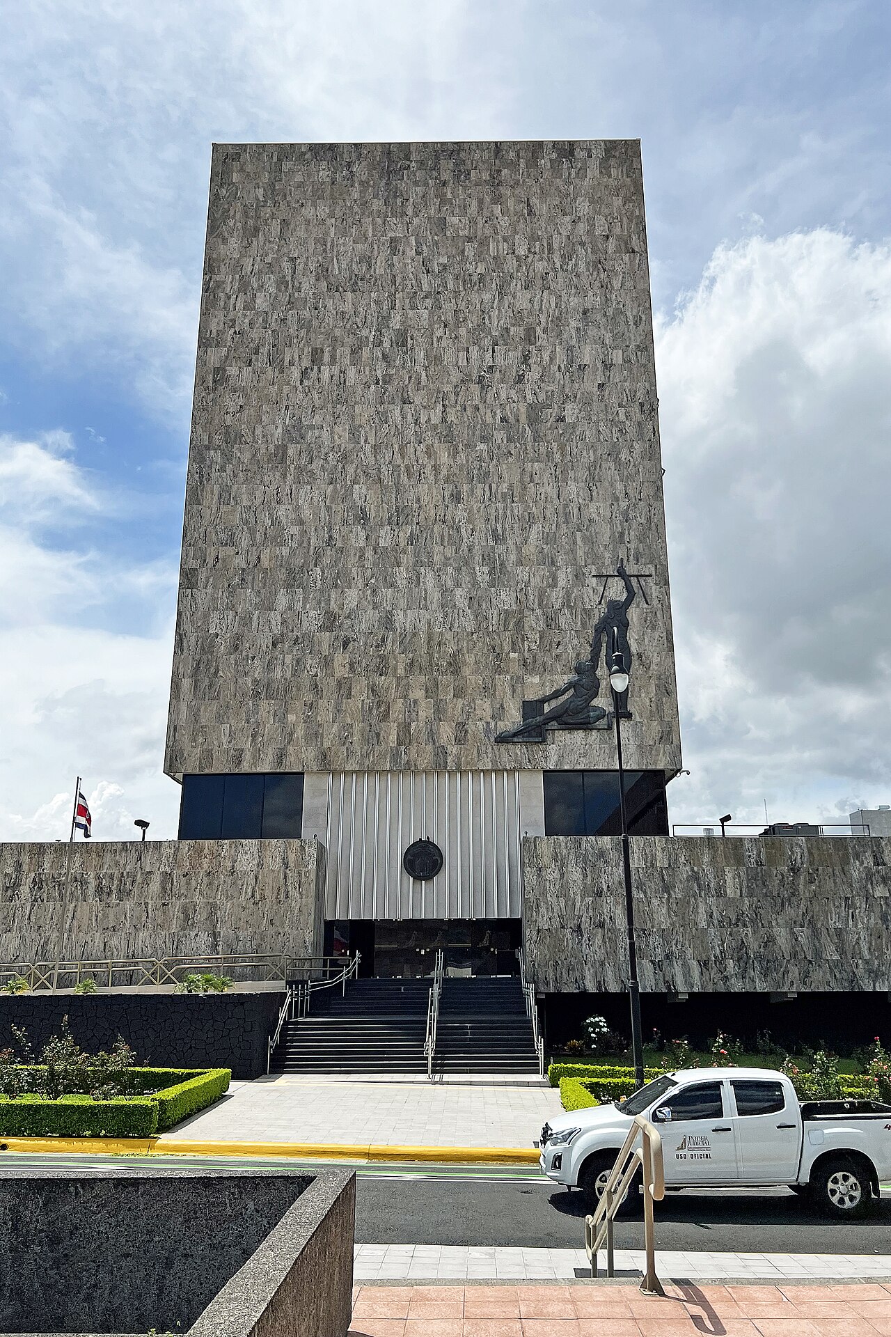 The stone-clad tower of Costa Rica's Supreme Court of Justice in San José, with the national flag and an official judiciary pickup truck outside