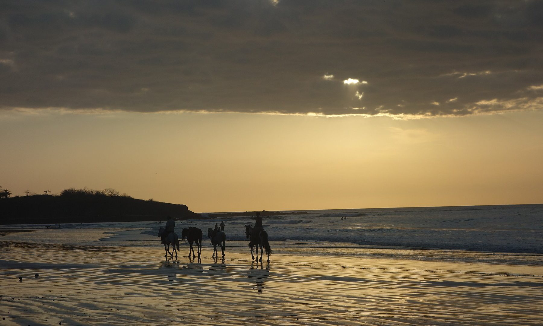 Costa Rica weather: horse riders on Tamarindo beach in Guanacaste at dusk under dry-season clouds in March
