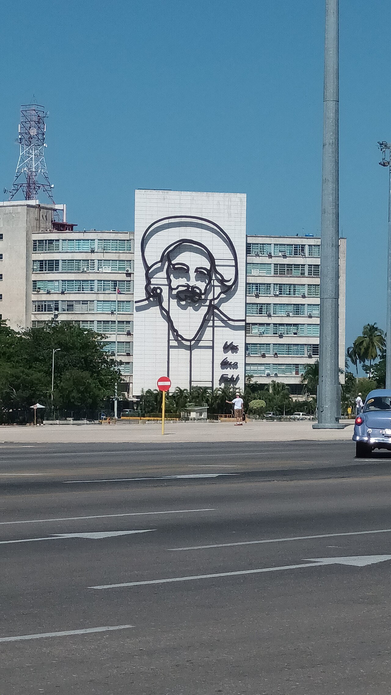 Steel outline of Camilo Cienfuegos on a ministry building at Plaza de la Revolución in Havana, with a vintage car in the street