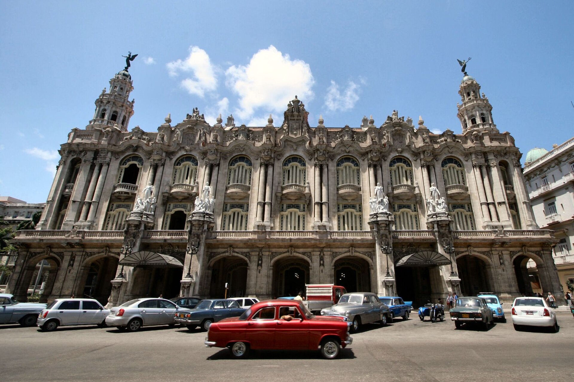 The ornate stone facade of the Gran Teatro de La Habana Alicia Alonso under a blue sky with a red classic car in the foreground