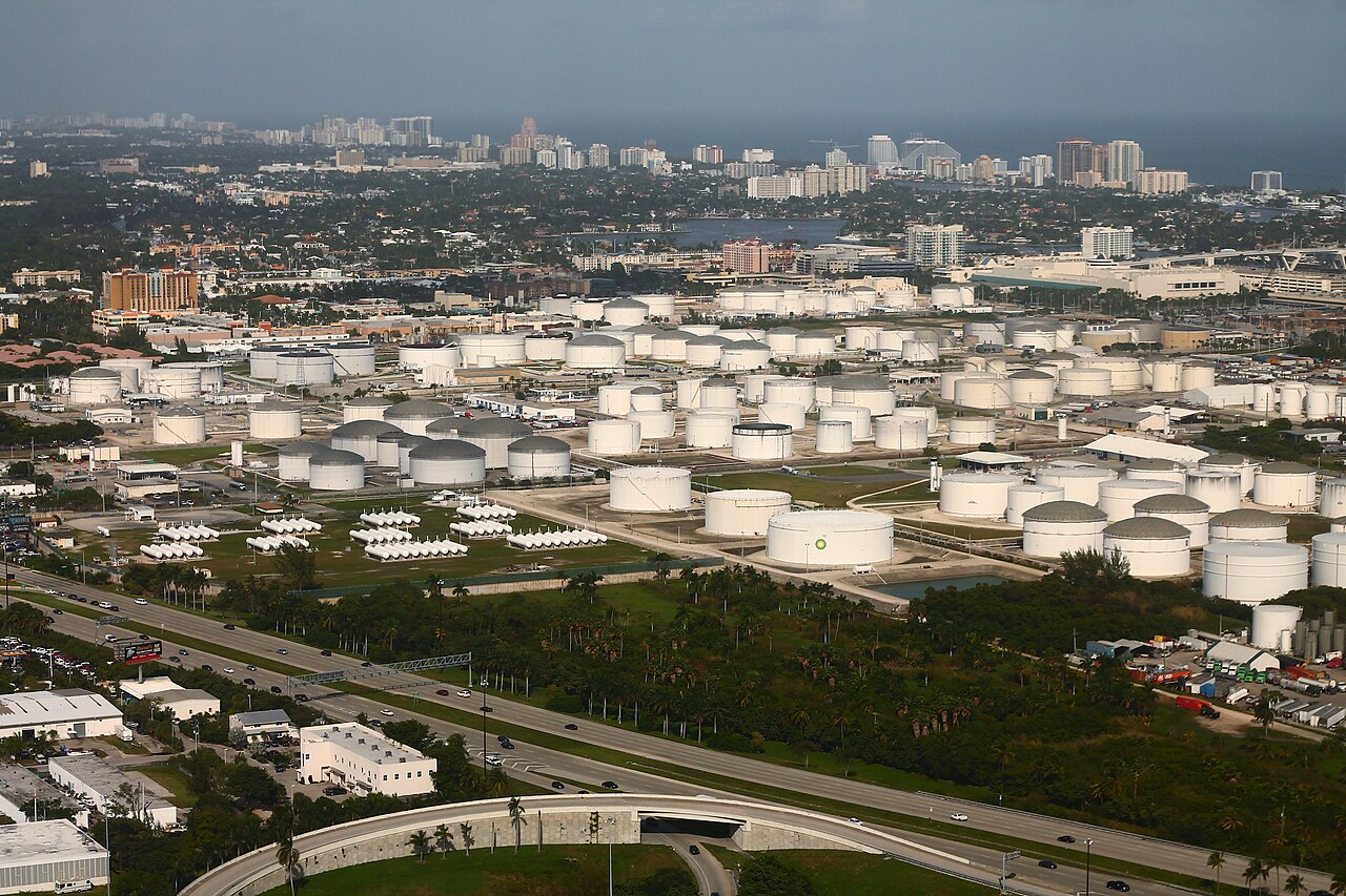 Aerial view of white fuel storage tanks at Port Everglades, Florida, with the Fort Lauderdale skyline behind