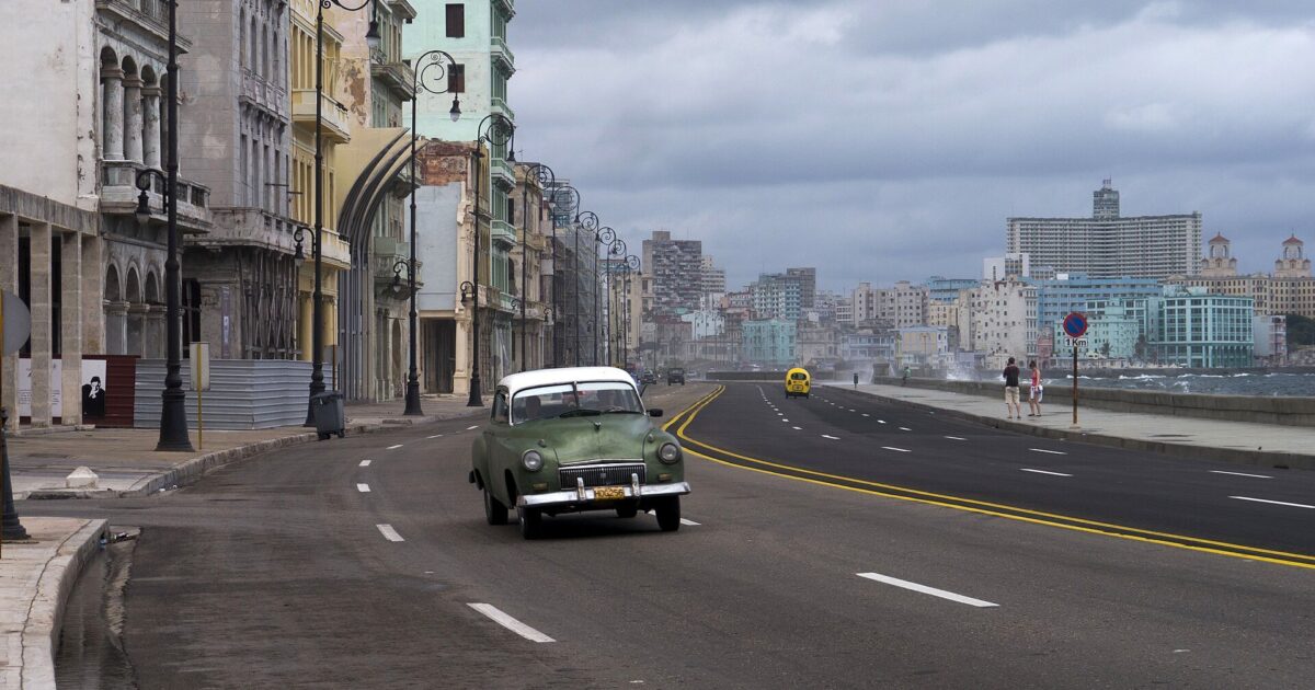 A vintage car drives along the Malecón seafront in Havana, Cuba, under a cloudy sky