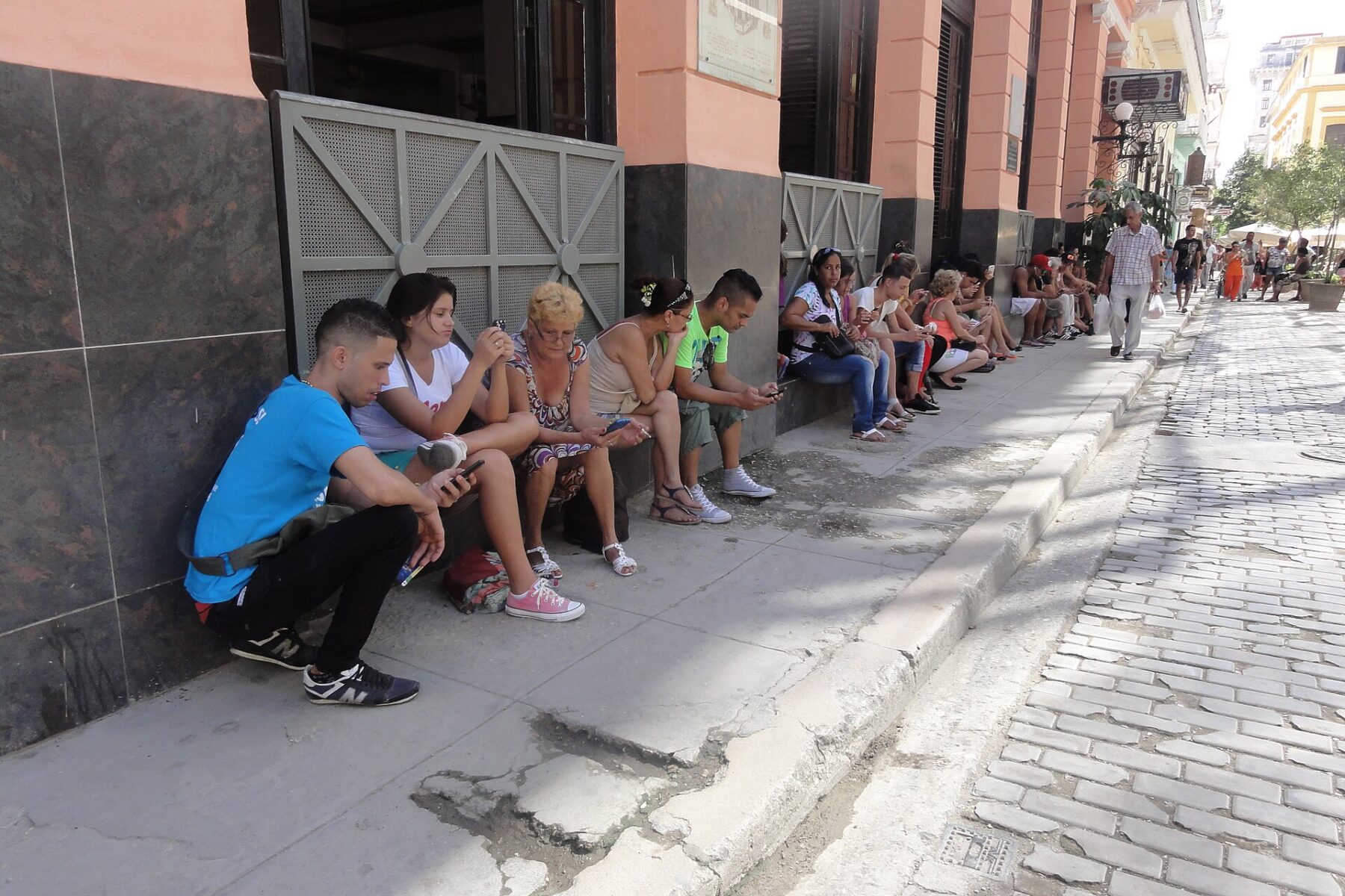 People sit on a pavement in Old Havana using their mobile phones at a public Wi-Fi spot