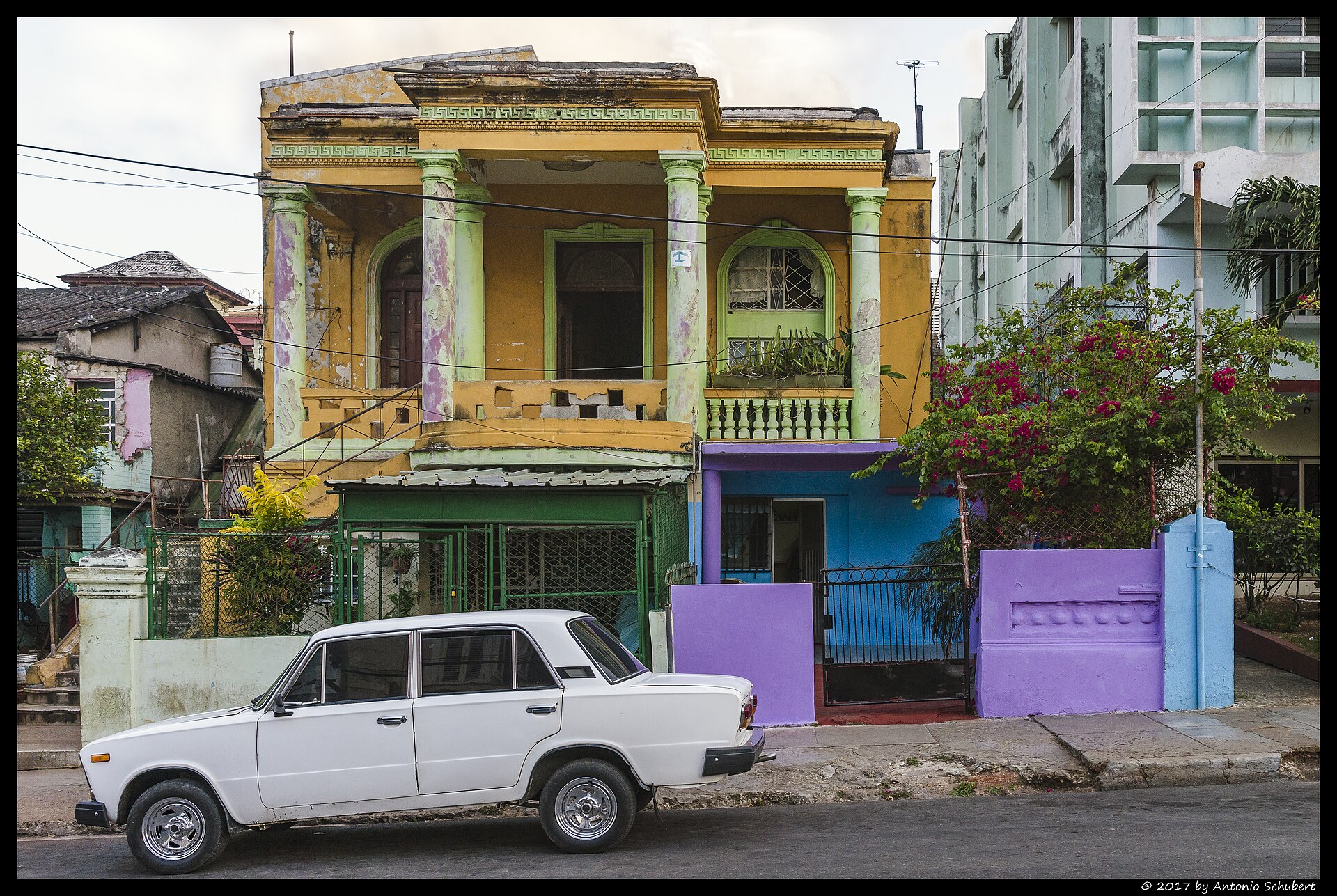A two-storey yellow house with columns and balconies beside a newer apartment block in the Vedado district of Havana