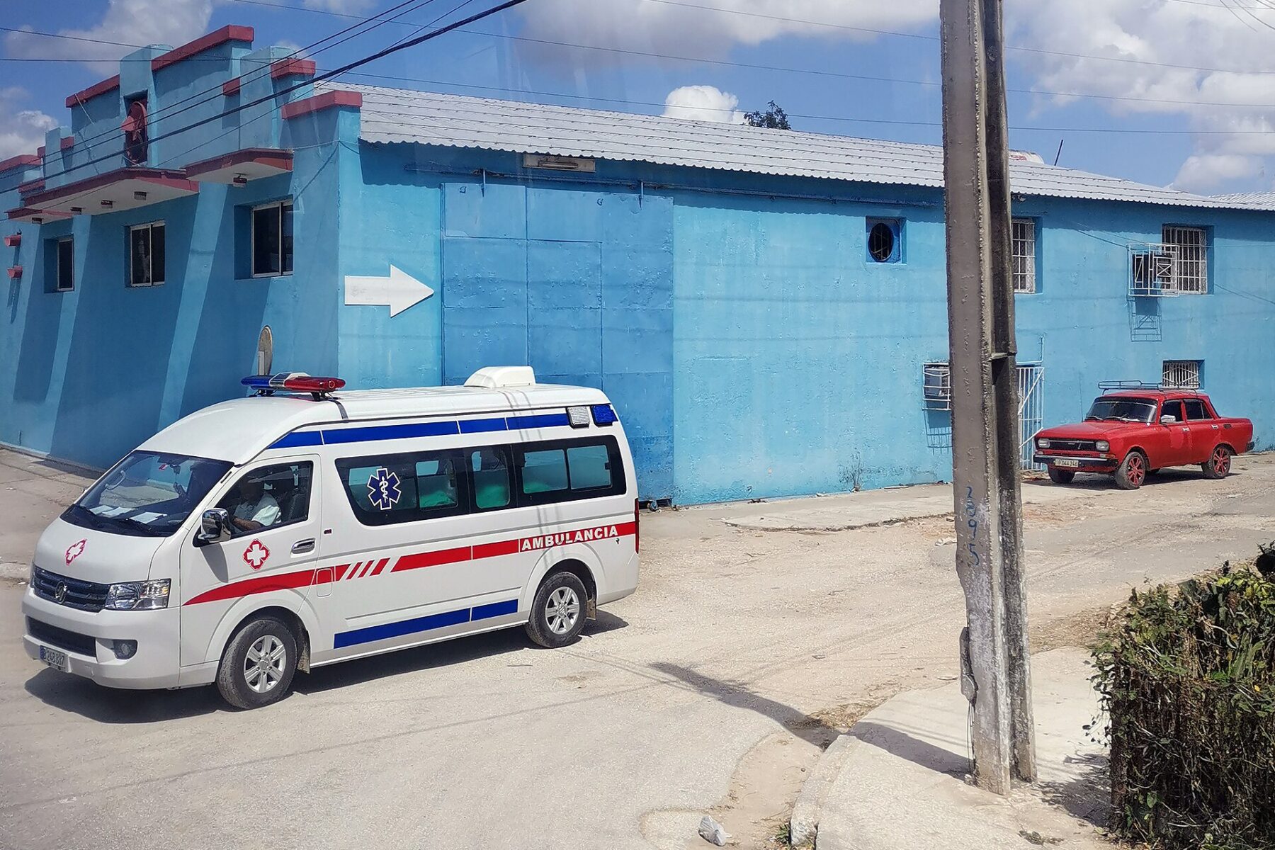 An ambulance drives past a blue building on a street in Cuba