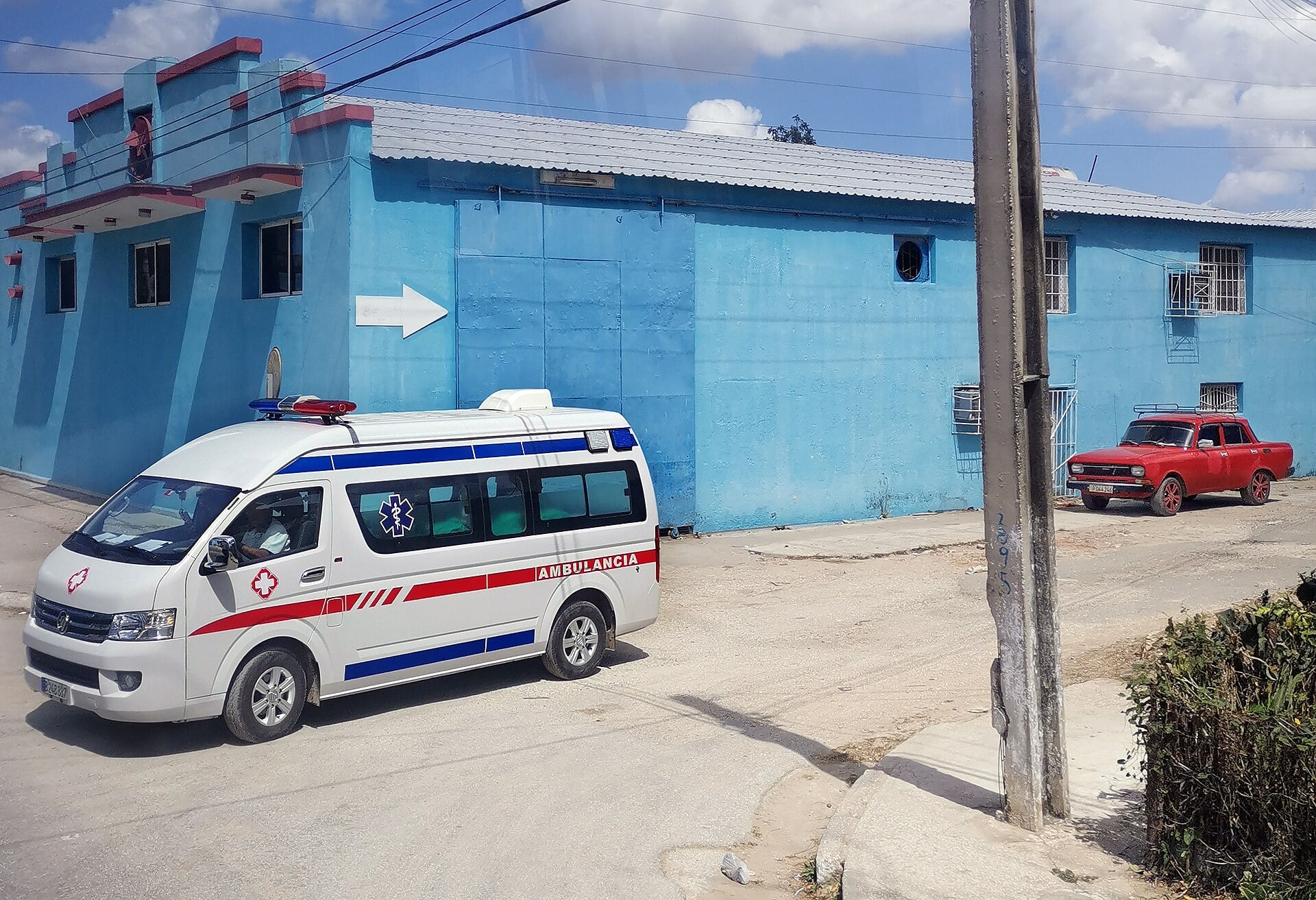 An ambulance drives past a blue building on a street in Cuba