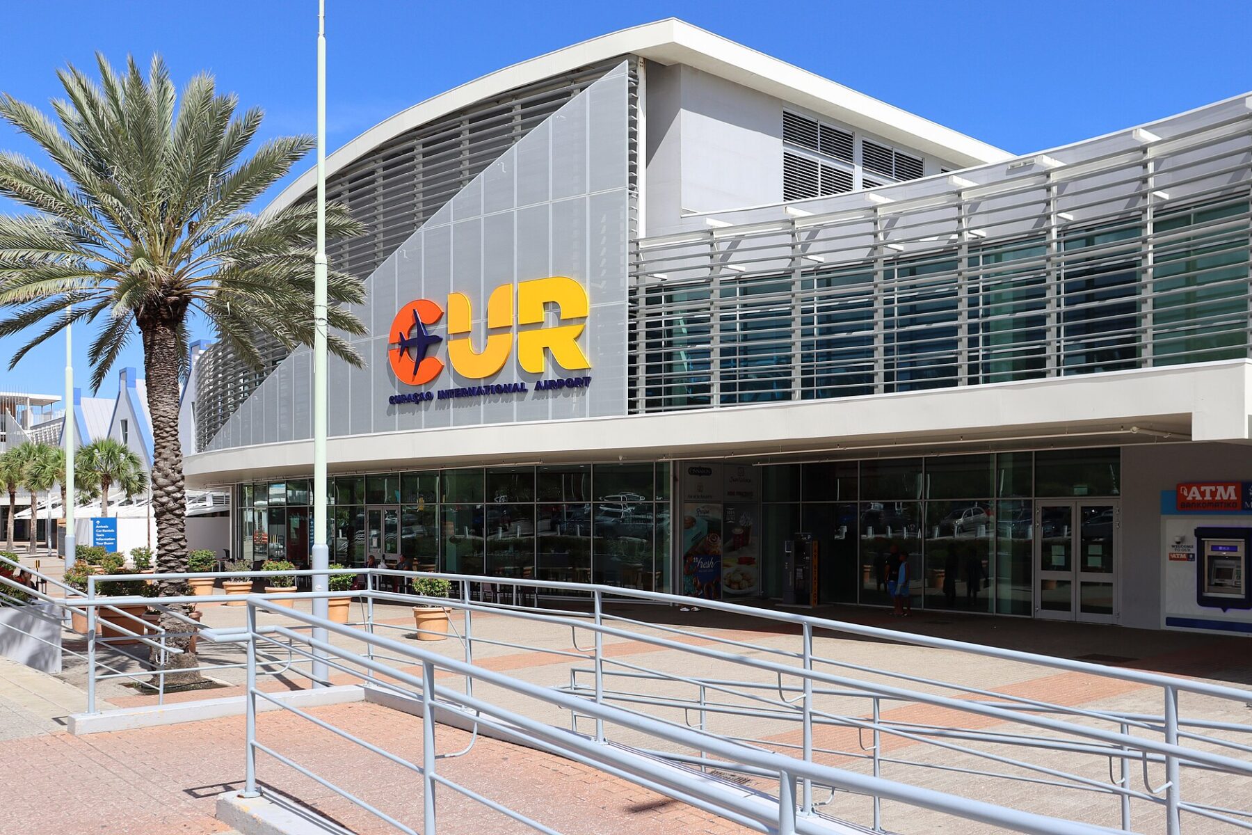 Exterior of the new terminal building at Curaçao International Airport with the CUR sign and a palm tree
