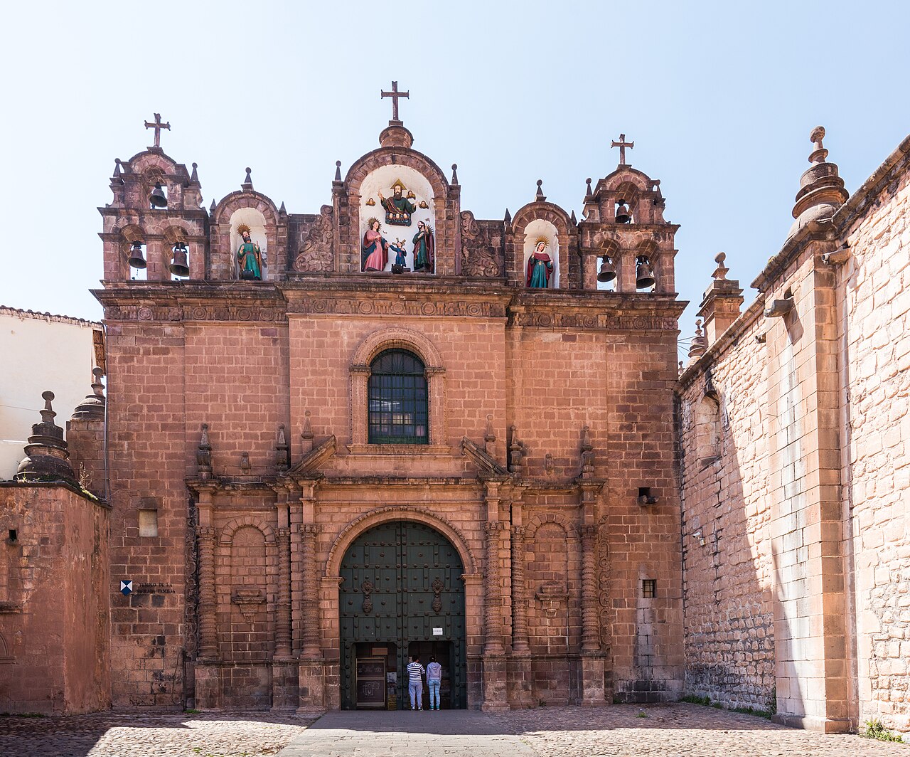 Red-stone baroque facade with bell towers and a green wooden door in the Cathedral complex on Cusco's Plaza de Armas