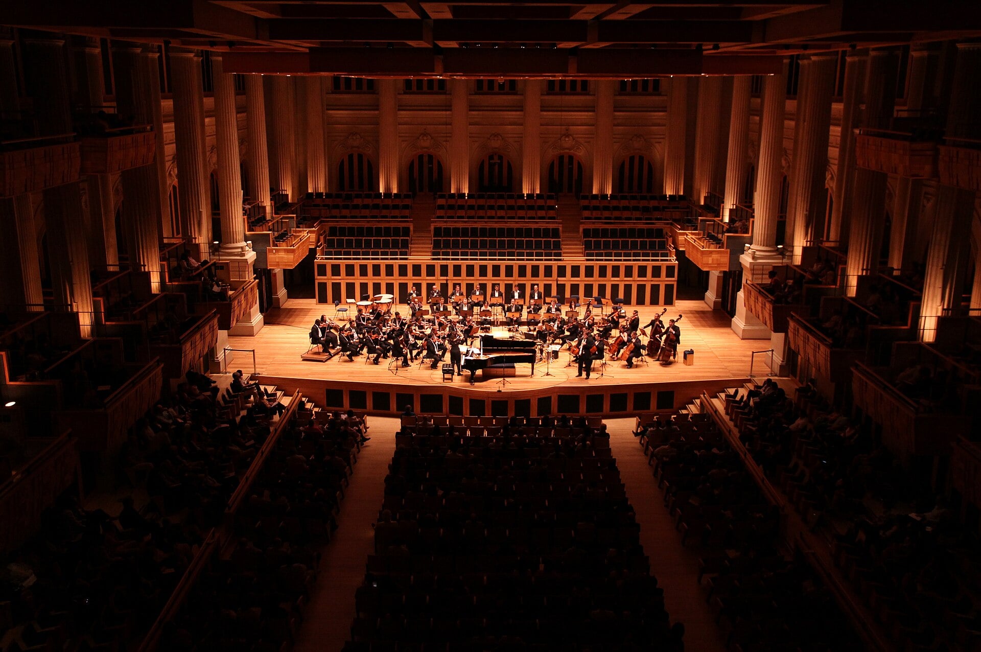 An orchestra on stage at Sala São Paulo seen from the back of the hall, with the stalls, side boxes and choir seats behind the stage