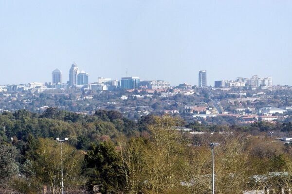 Distant skyline of Sandton, the business district of Johannesburg, rising above trees under a pale blue sky