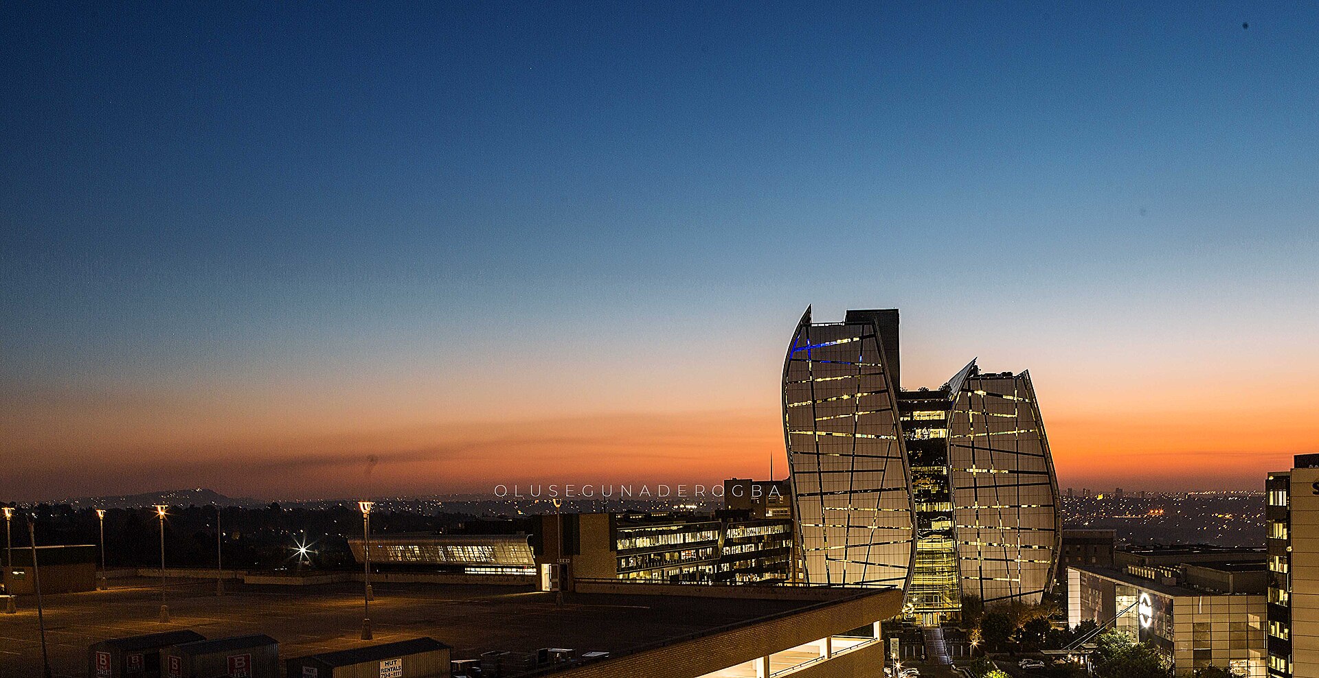 Glass office towers in Sandton, Johannesburg, lit up at dusk under an orange and blue sky