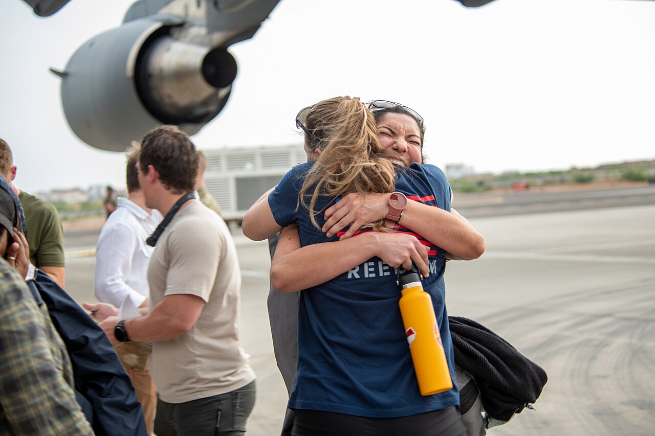 Two people embrace on the airfield at Camp Lemonnier beside the engine of a transport aircraft