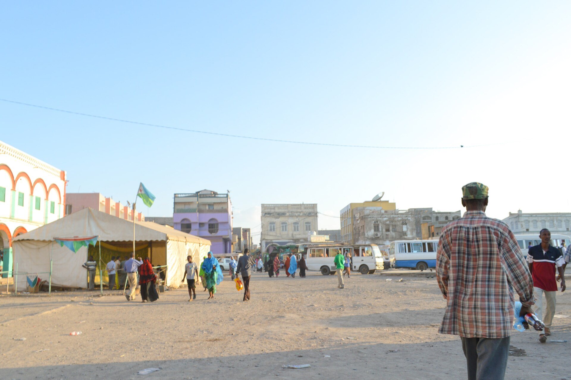 Pedestrians and minibuses at Place Rimbaud, a square in Djibouti City, under a clear sky