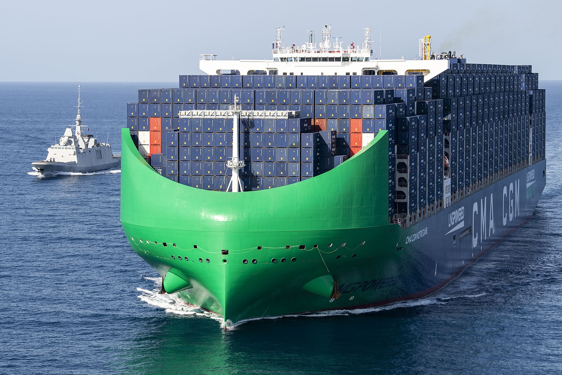 A French Navy frigate escorts a large green-bowed CMA CGM container ship through the Bab el-Mandeb strait