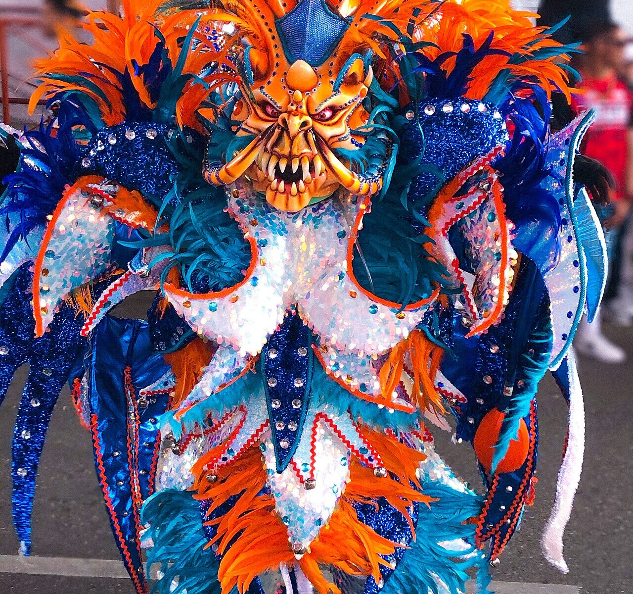 A diablo cojuelo carnival character in an orange and blue feathered costume and fanged mask during the La Vega carnival in the Dominican Republic.