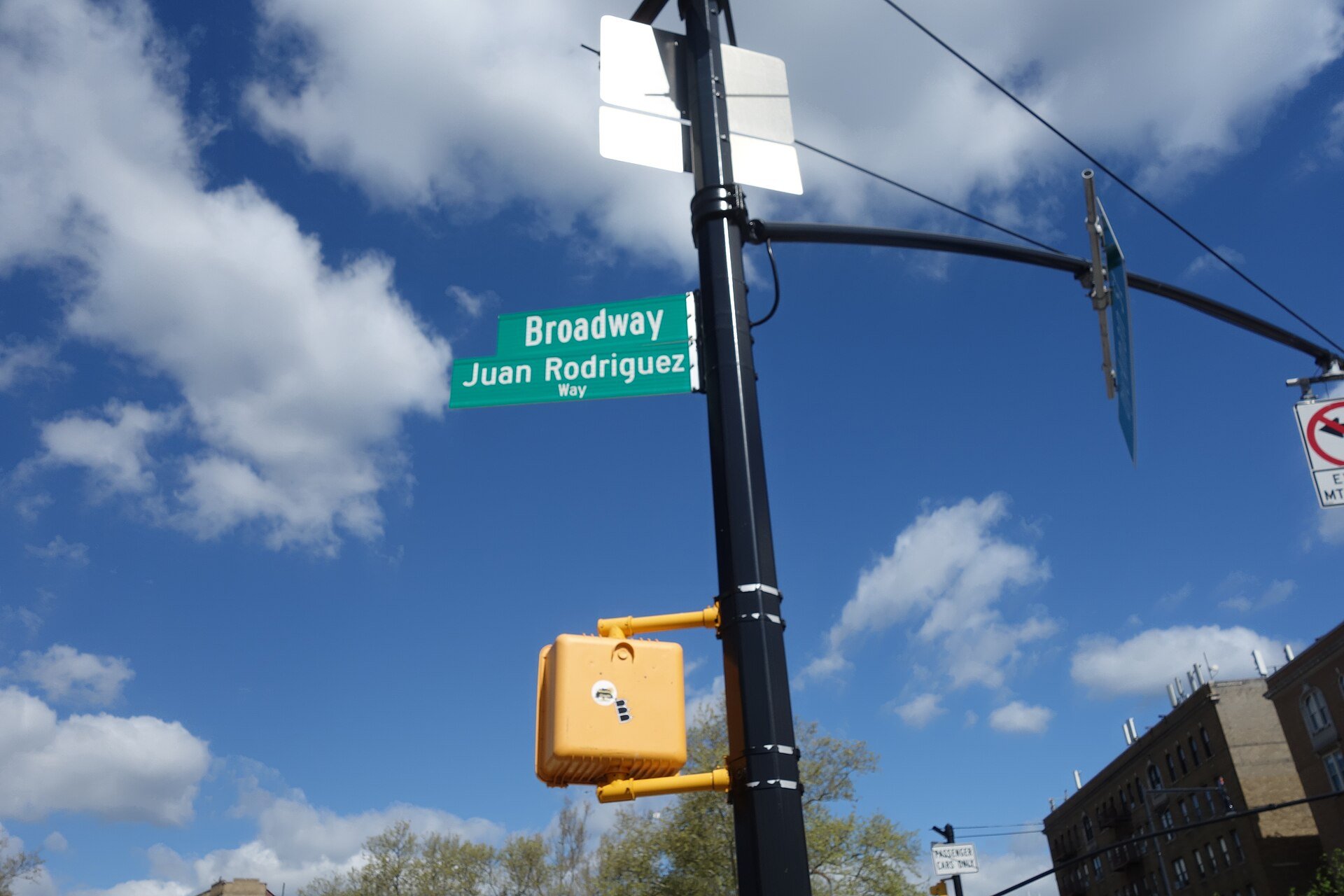 Green street sign reading Broadway and Juan Rodriguez Way against a blue sky in Inwood, Upper Manhattan