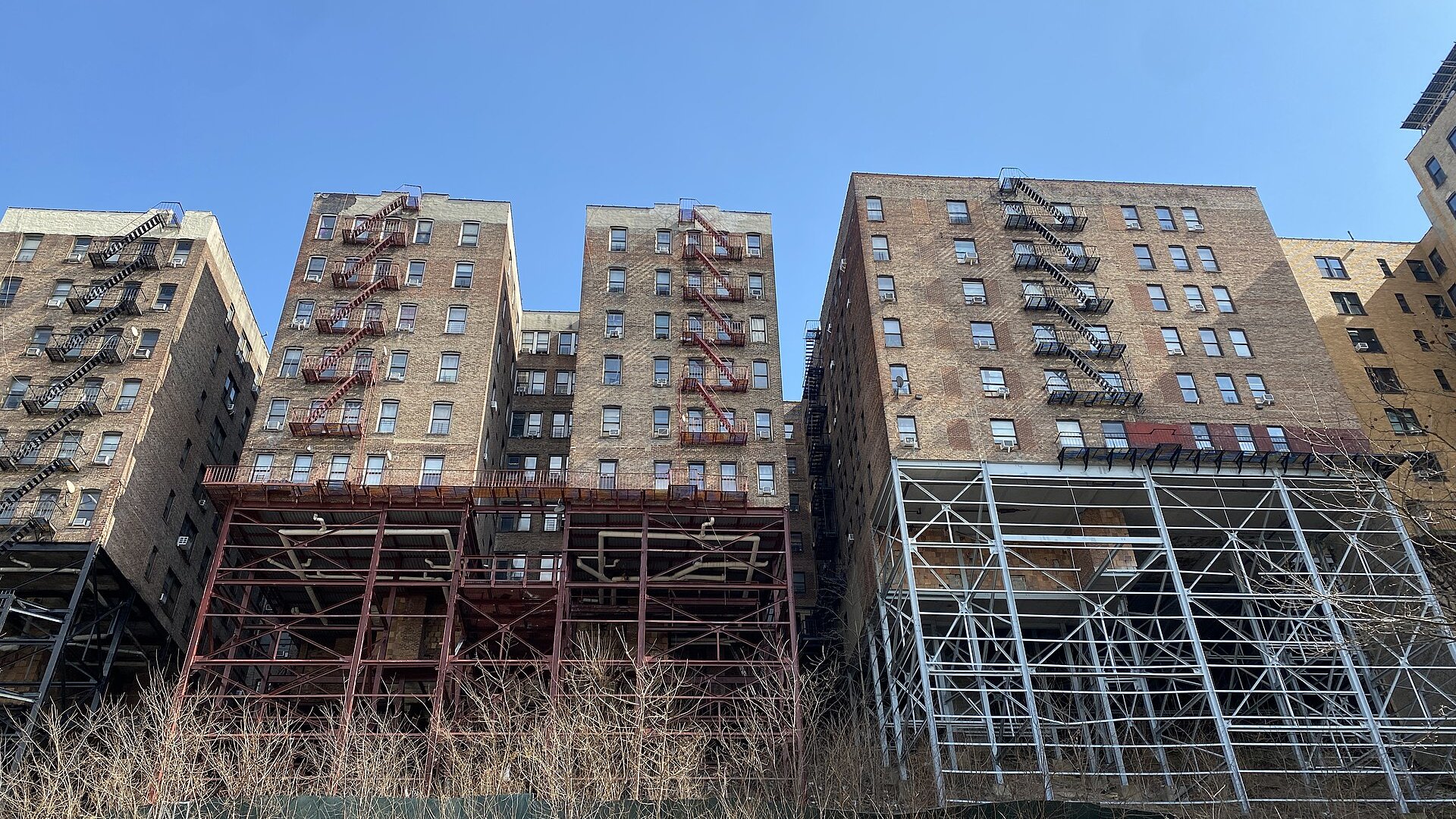 Brick apartment buildings with fire escapes rising above steel supports on Fairview Avenue in Washington Heights, Manhattan