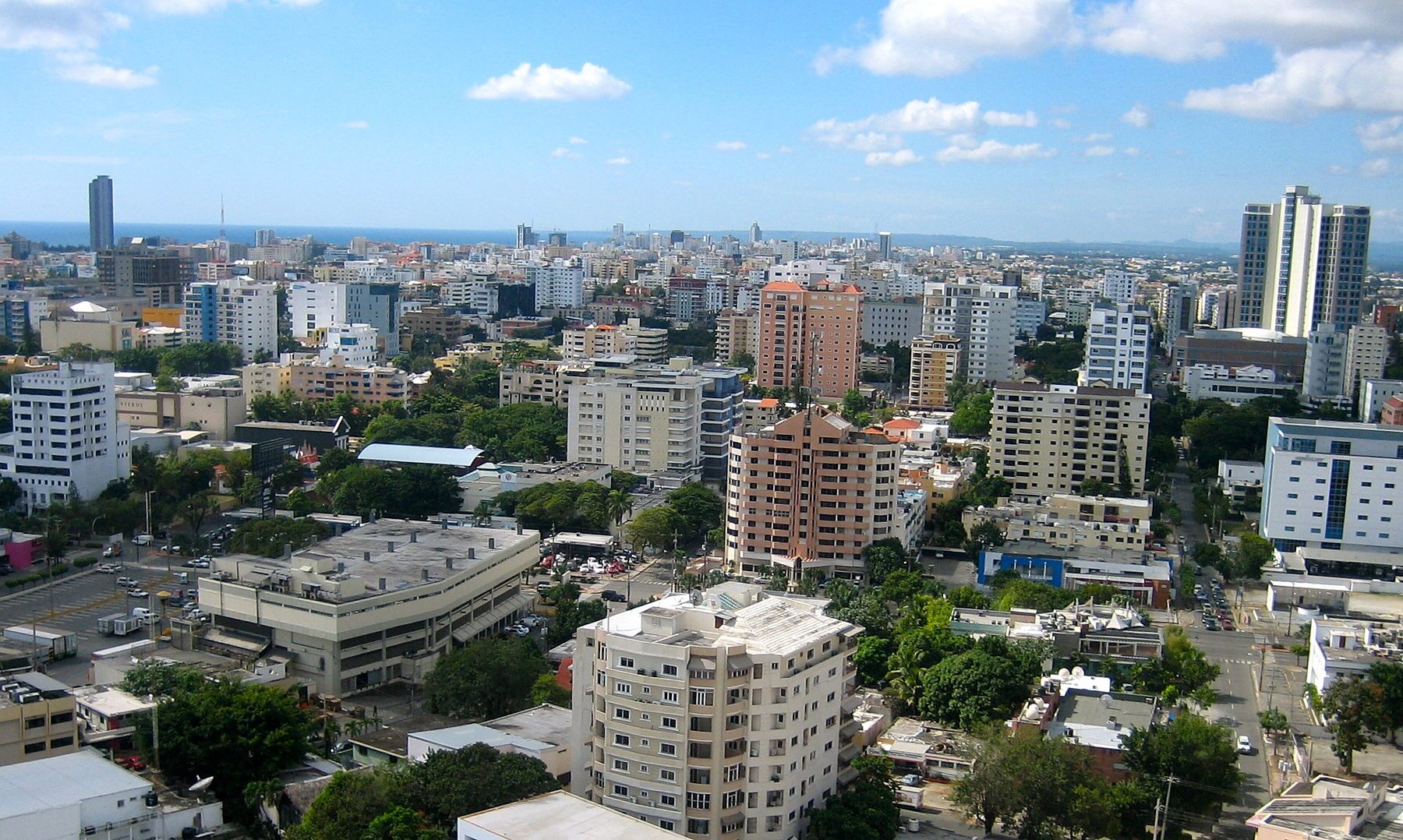 A view over the buildings of Santo Domingo with the Caribbean on the horizon under a blue sky with scattered clouds
