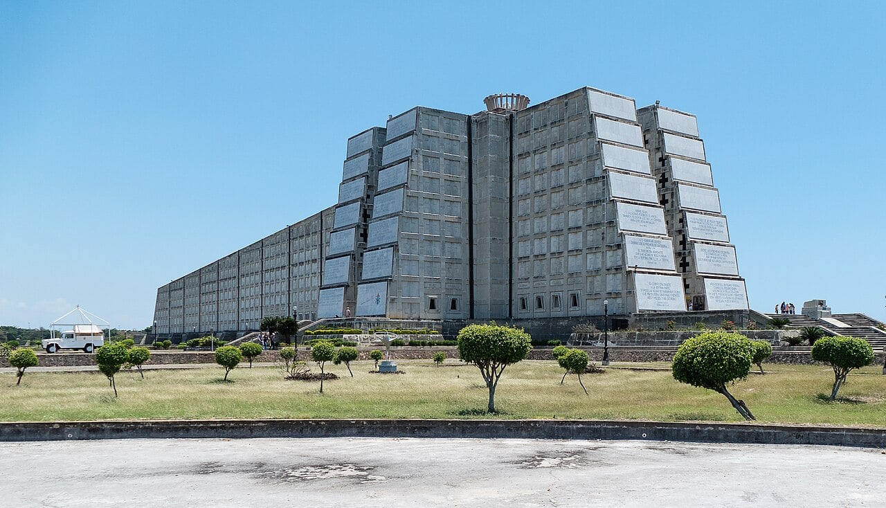 The long, stepped concrete monument of the Columbus Lighthouse in Santo Domingo Este, with trimmed trees on a lawn in front