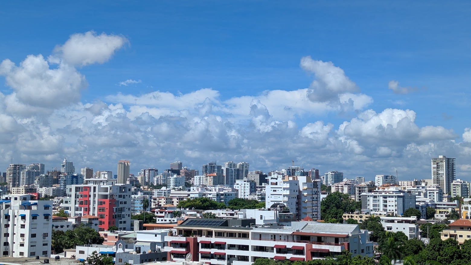 Apartment towers and trees of the La Esperilla district under a blue sky with clouds in Santo Domingo, Dominican Republic
