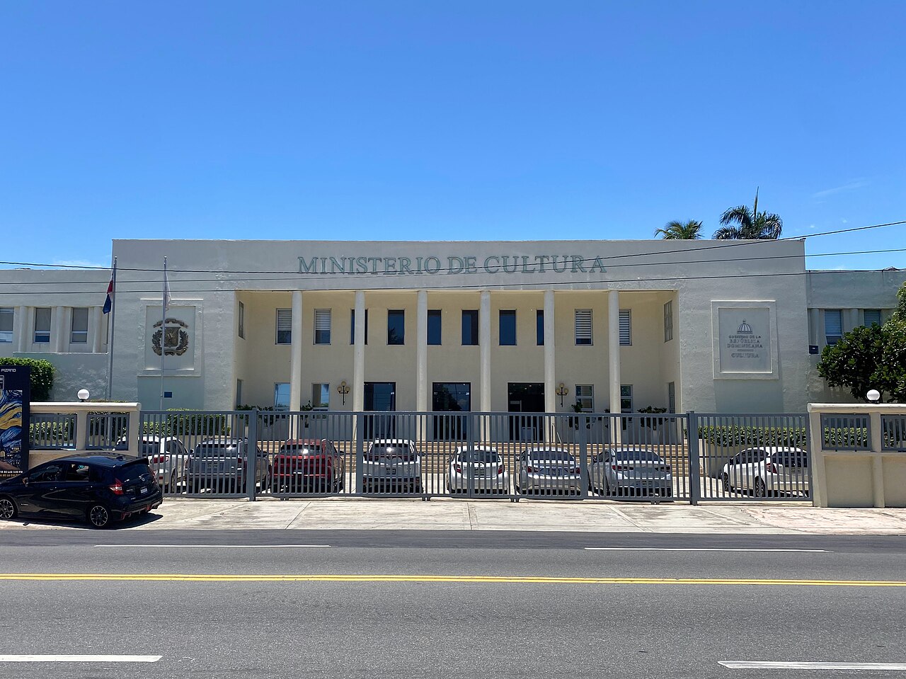 The white, columned front of the Ministry of Culture building in Santo Domingo, with cars parked behind a fence